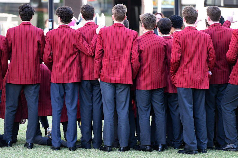 Private school boys stand in a line with their backs to the camera.