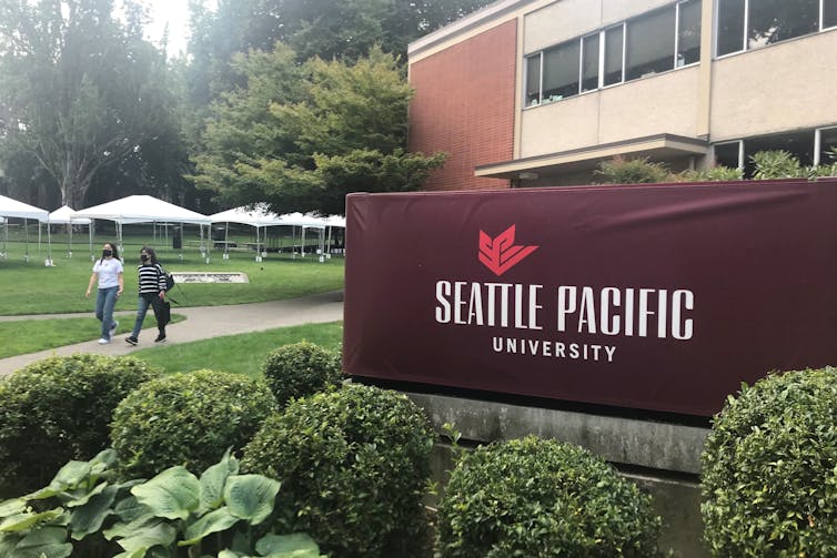 Two students walk down a sidewalk near a sign that says, 'Seattle Pacific.'