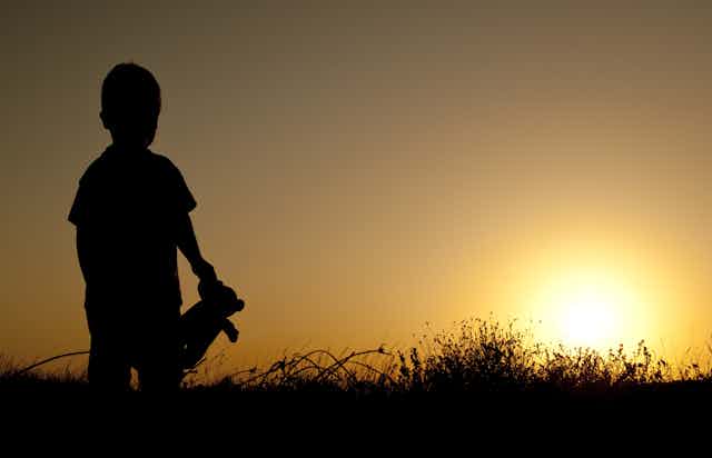 Silhouette of child with teddy bear standing looking at sunset