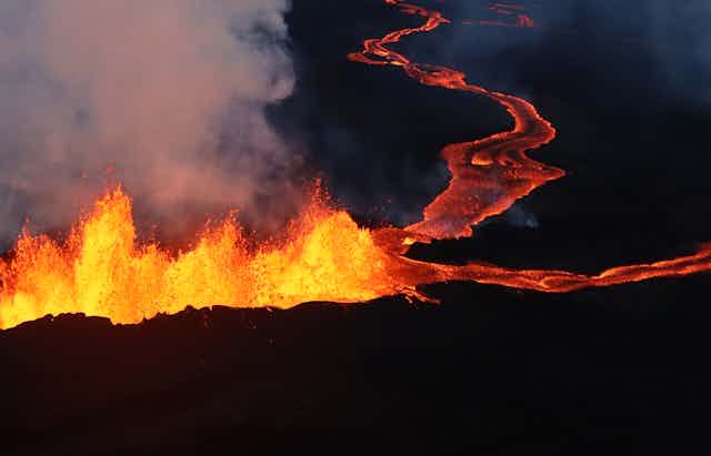 A line of lava fountaining upward and flowing, with steam rising.