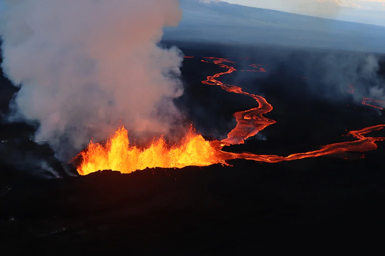 A line of lava fountaining upward and flowing, with steam rising.