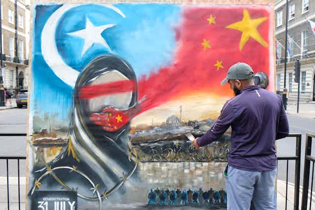 A man paints an image of a silenced Uyghur Muslim woman oin a wall in London.