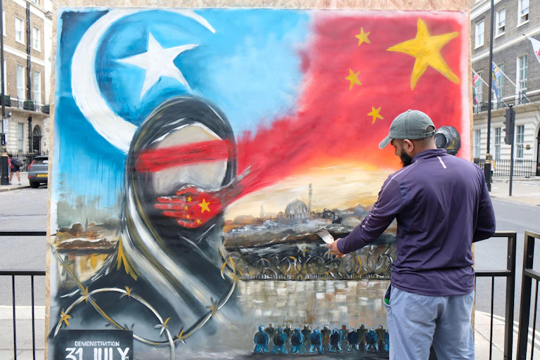 A man paints an image of a silenced Uyghur Muslim woman oin a wall in London.