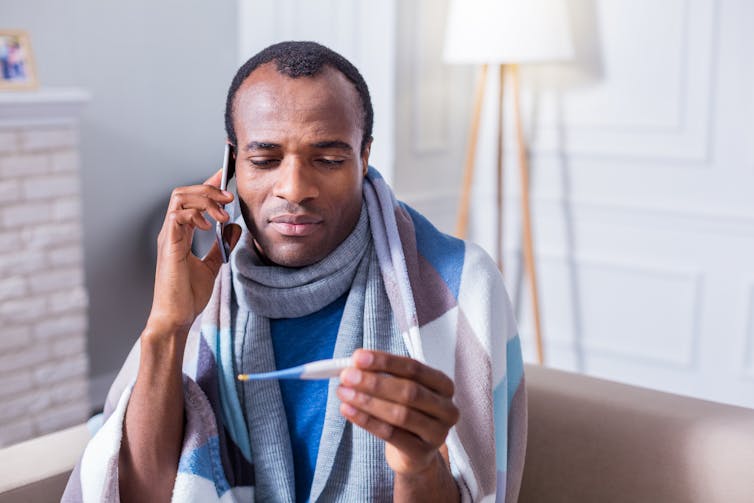 A man on the phone looks at a thermometer.