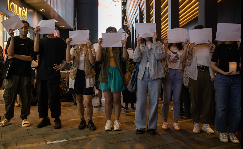 A line of people holding white pages in front of their faces.