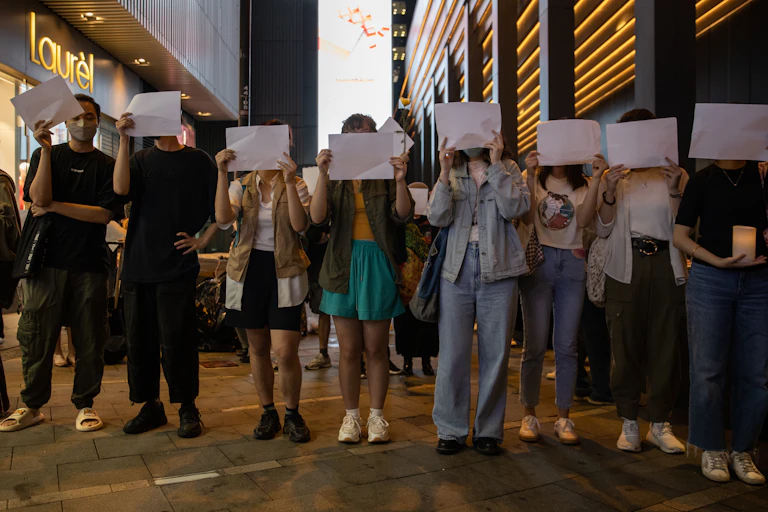 A line of people holding white pages in front of their faces.