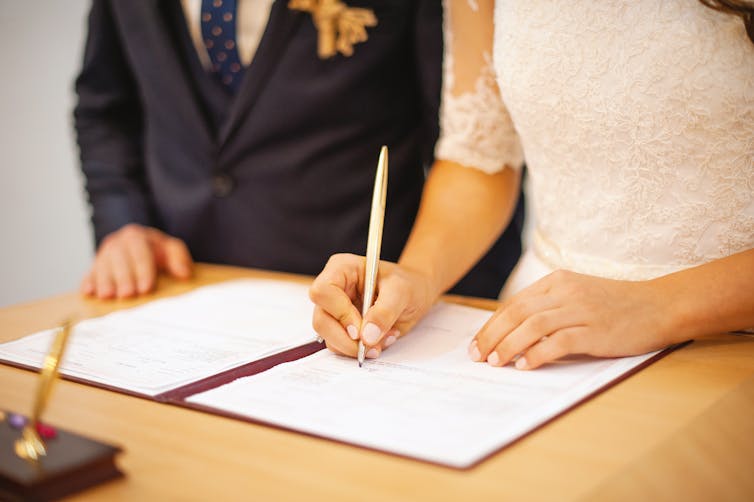 A woman wearing a white dress signing a contract.