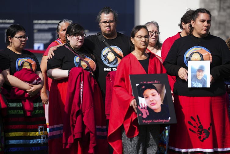 A group of people wearing red and holding photos of women.