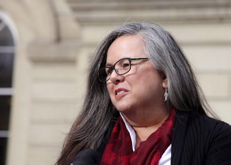 A woman wearing glasses and a red scarf with long grey hair.