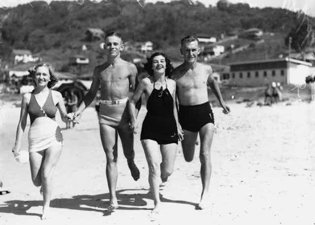 Two men and two women run on a beach