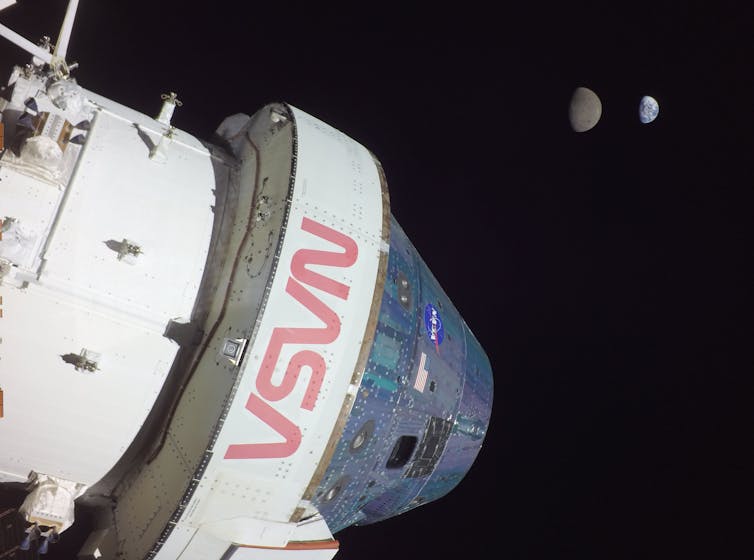 A photo showing a white spacecraft in the foreground, with the Moon and Earth in the background.