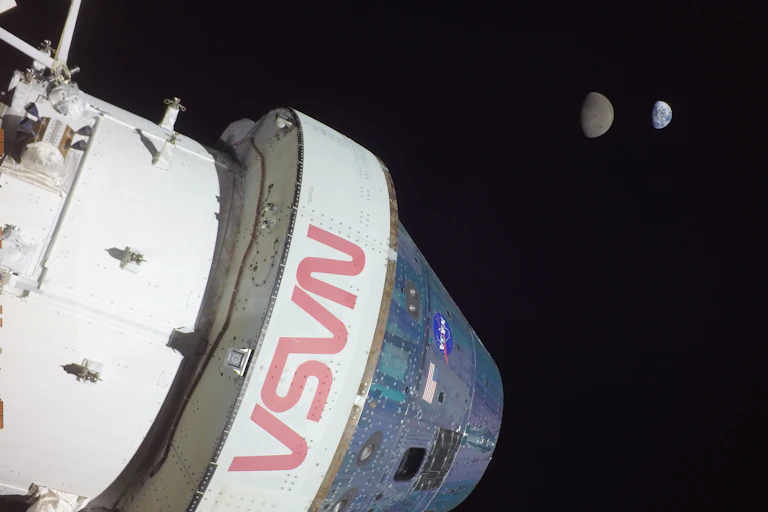 A photo showing a white spacecraft in the foreground, with the Moon and Earth in the background.
