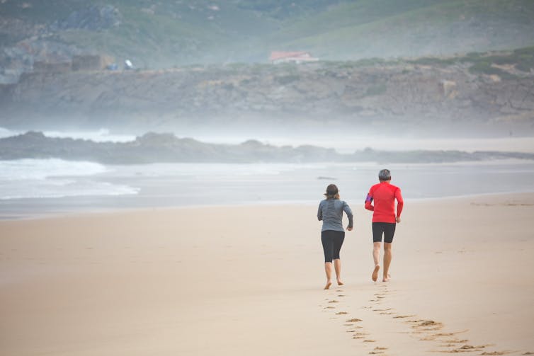 Two people run barefoot on a beach.