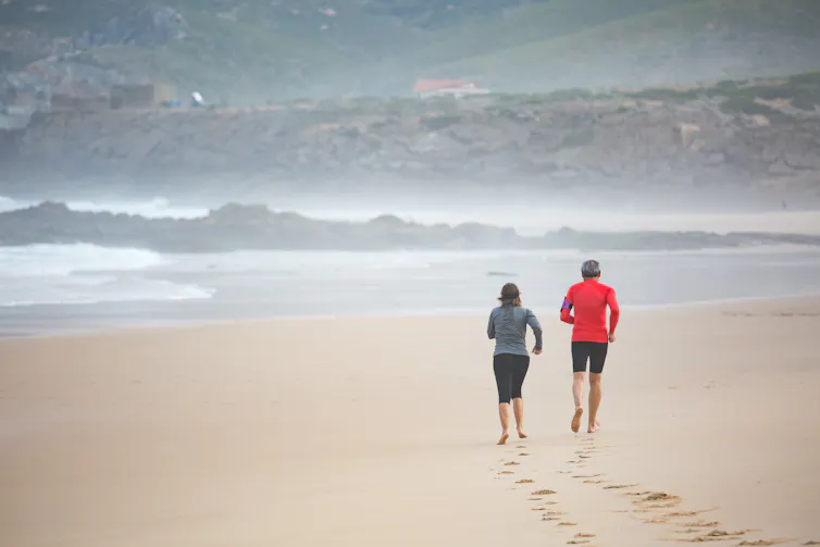 Two people run barefoot on a beach.
