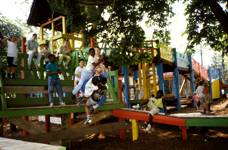 Children crowd on to a swing on a colourful playground structure