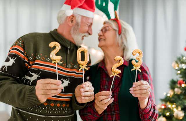 older man and woman look into each other's eyes, holding 2023 balloons