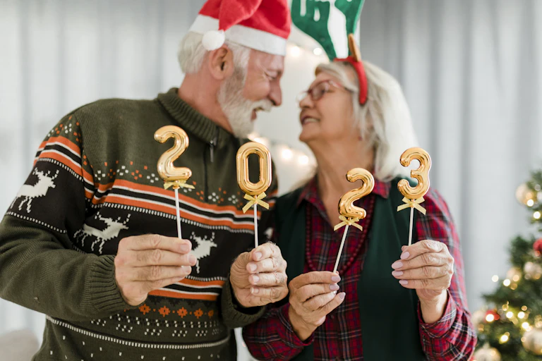 older man and woman look into each other's eyes, holding 2023 balloons