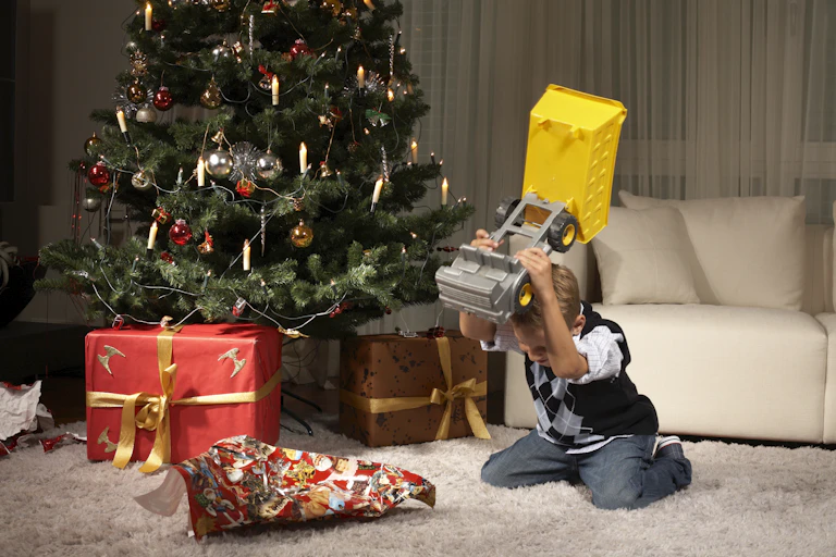 Young boy in sweater smashes his toy truck into the carpet.
