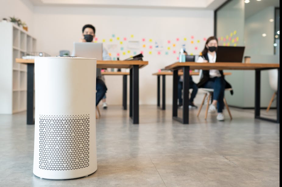 An air purifier in the foreground, people working in the background.