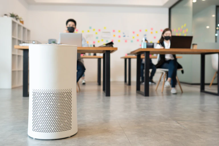An air purifier in the foreground, people working in the background.