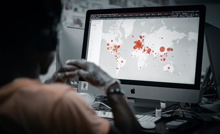 A person looks at a laptop displaying a world map with red hotspots.