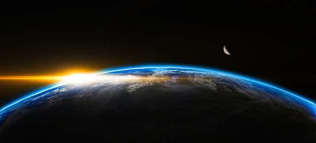 A shot of a space sunset on planet Earth with a cresent moon visible.