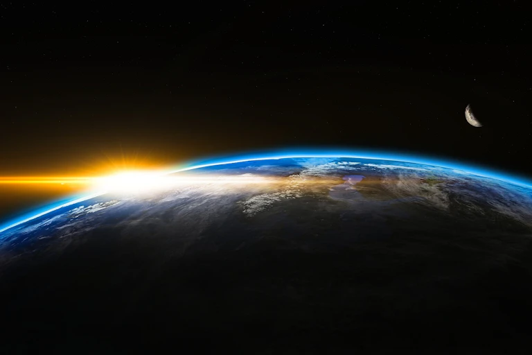 A shot of a space sunset on planet Earth with a cresent moon visible.