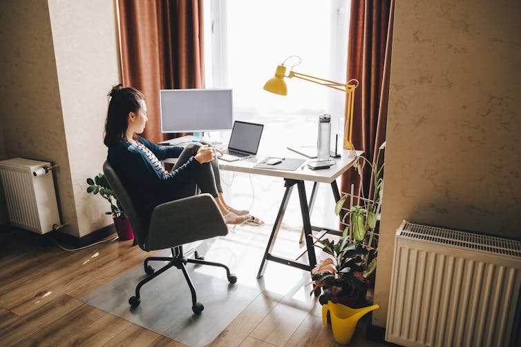 A young woman, sitting at a computer, facing a window