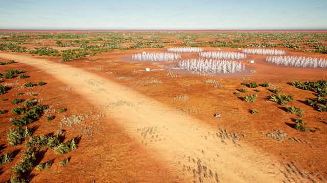 Aerial view of a dirt road in a red desert, with fields of antennae. 