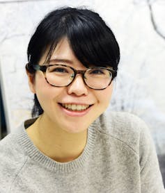 A young Japanese woman with tortoiseshell glasses smiling at the camera