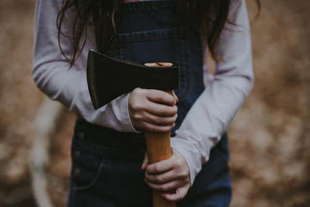 a girl in overalls holding an axe