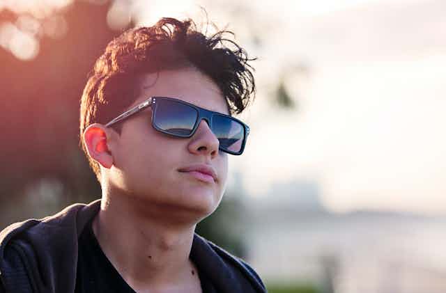 Portrait of teenager wearing sunnies, with neutral expression.