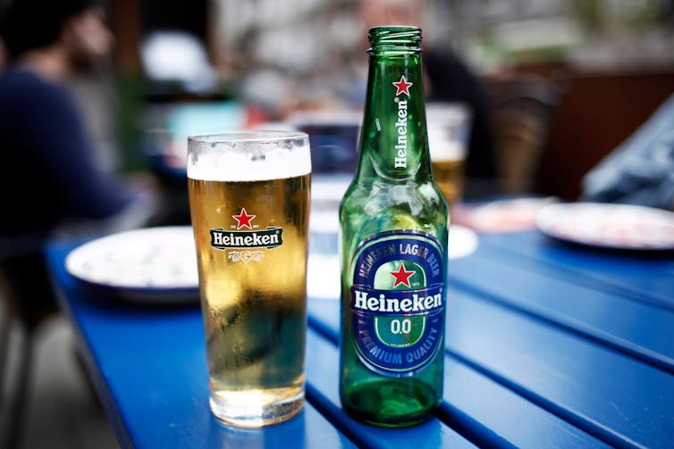 A Heineken 0% beer bottle and glass of beer with the Heineken label on a blue table