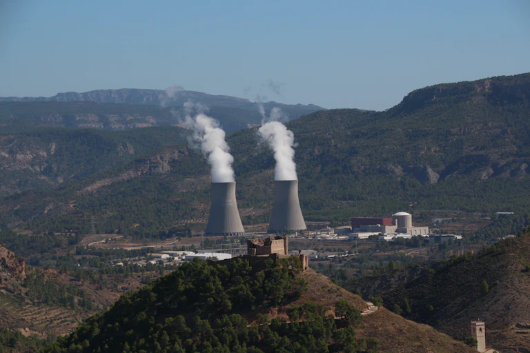 Chimeneas echando humo blanco rodeadas de un paisaje montañoso.