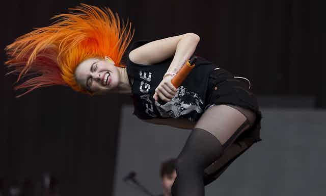 Hayley Williams of Paramore performs on stage, head banging with her bright orange hair flying.