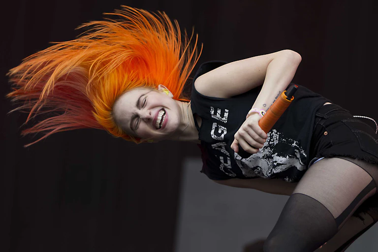 Hayley Williams of Paramore performs on stage, head banging with her bright orange hair flying.