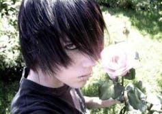 An 'emo boy' takes a selfie holding a pink rose. His dyed black hair is swept across his face, and he wears black eyeliner.