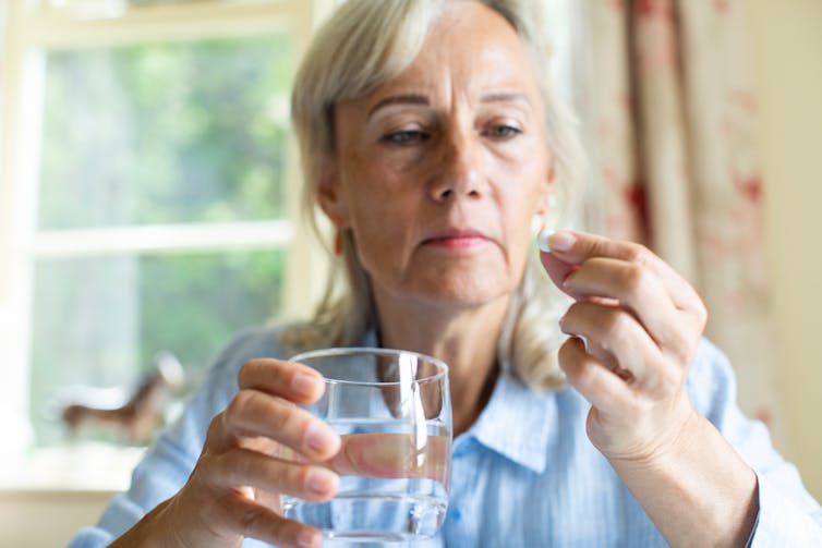 A woman holds a glass of water and a tablet.