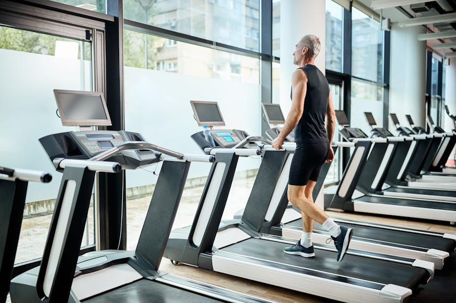 A middle-aged man walks on a treadmill on the gym.