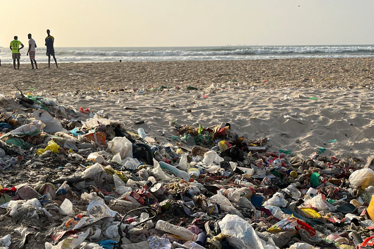 Boys standing on the beach shore backing a heap of plastic waste.