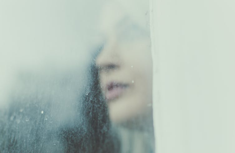 A woman looks through a rainy window.