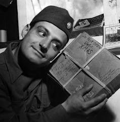 A man in a soldier's cap shakes a wrapped package that says 'Do not open until XMAS.'