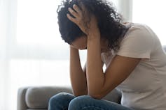 A woman in a white T-shirt and jeans sits with her head in her hands.
