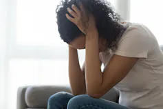 A woman in a white T-shirt and jeans sits with her head in her hands.