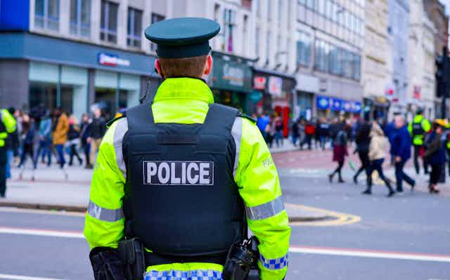 The back of a policeman wearing a green hat, protective vest and high visibility jacket.