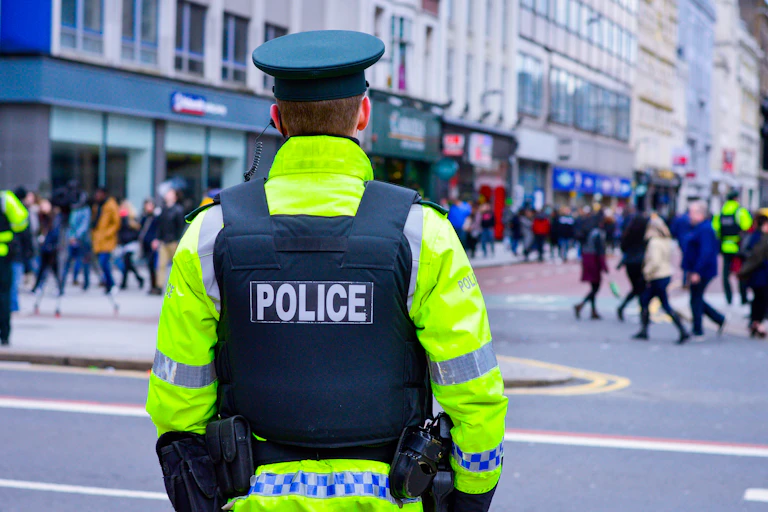The back of a policeman wearing a green hat, protective vest and high visibility jacket.