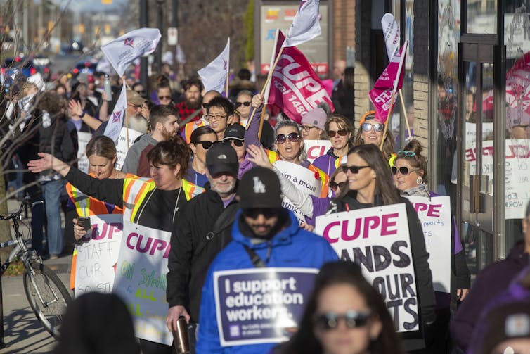 A crowd of people holding CUPE signs and flags marching down a sidewalk
