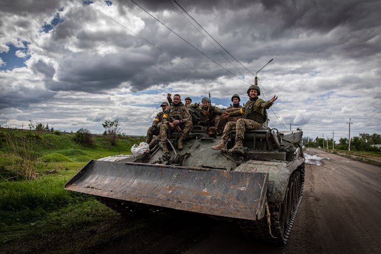 A group of soldiers are sitting atop an armoured vehicle.