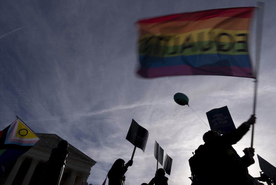 A rainbow flag with 'equality' written backwards is held aloft in front of the Supreme Court.