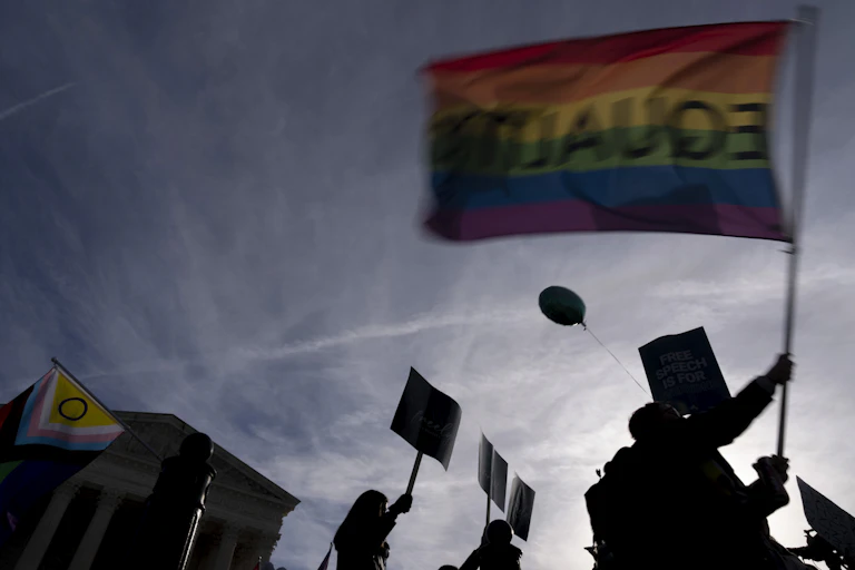 A rainbow flag with 'equality' written backwards is held aloft in front of the Supreme Court.